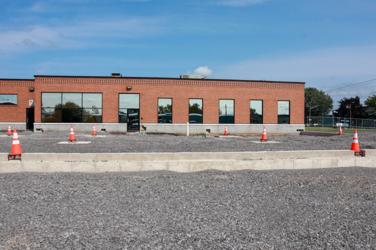 Gravel and concrete foundation outside a Sealing Devices brick office building during expansion construction.