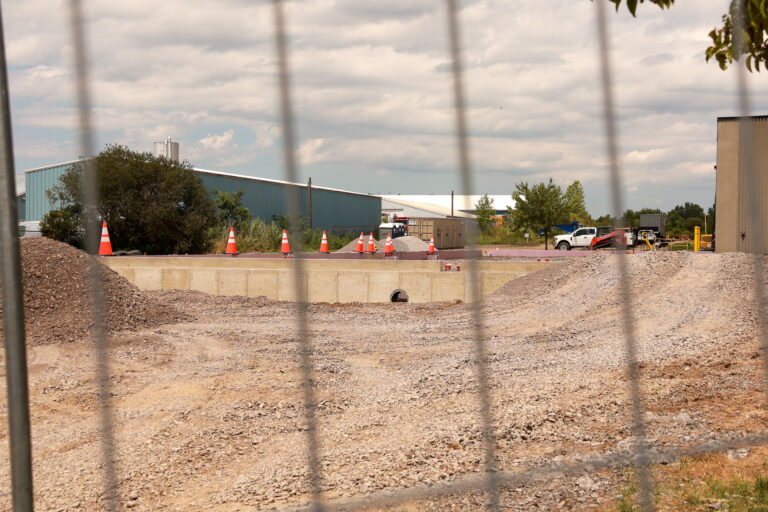 Concrete foundation walls and gravel viewed through fencing at the Sealing Devices construction site.