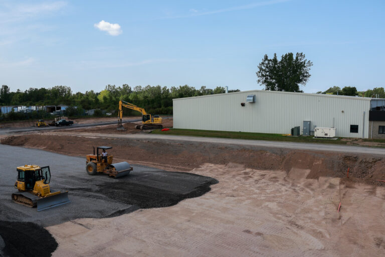 Aerial view of a bulldozer, road roller, and excavator preparing the Sealing Devices expansion site.