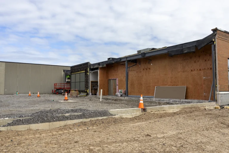 Exterior wall under renovation with exposed plywood, steel columns, and concrete foundation walls in the foreground.