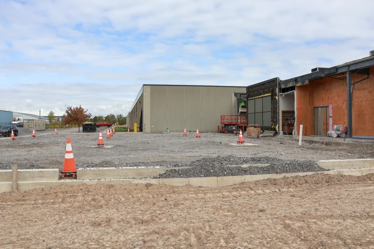 Wide view of the construction area with gravel fill, concrete foundation walls, and partially exposed building walls.