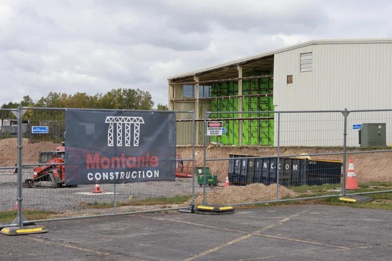Montante Construction banner on fencing in front of exposed building framing, green sheathing, and construction equipment.